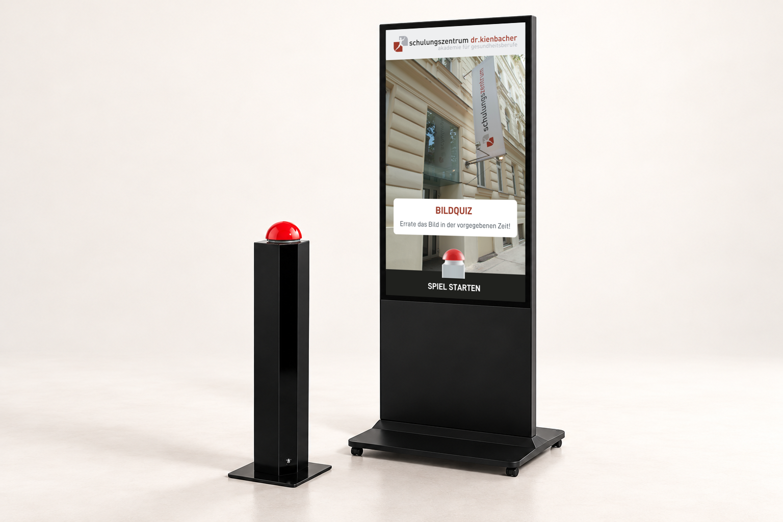 GAMIFY Bildquiz Setup: Hochformat-Kiosk mit Bildquiz im Branding des Schulungszentrums Dr. Kienbacher und daneben eine Buzzer-Stele mit rotem Buzzer